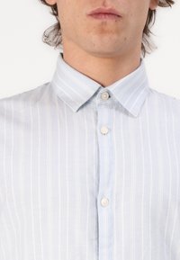 Camisa abotonada de color azul claro con rayas verticales blancas, cuello clásico y cierre de botones; hecha de una tela suave y tejida.