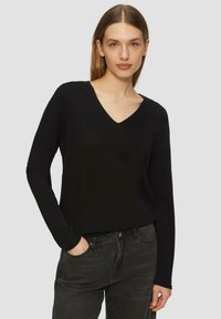 Zwarte V-hals trui van een zachte breimateriaal, met lange mouwen en een relaxte pasvorm, gecombineerd met donkere high-waisted jeans.