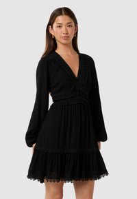 Abito nero con scollatura a V profonda, maniche lunghe e rifinitura in pizzo. Presenta volants sovrapposti e un tessuto testurizzato. Design semplice ed elegante.