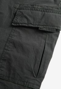 Black fabric cargo pant featuring a side flap pocket, visible stitching, and a textured surface. The design is sleek with clean lines.