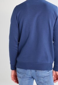 Navy blue sweatshirt with a crew neck and long sleeves, featuring a smooth texture and ribbed cuffs and hem, paired with light blue jeans.
