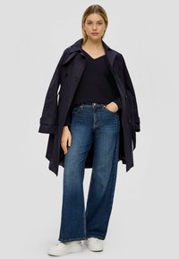 Marineblauer Trenchcoat über einem schwarzen V-Ausschnitt-Pullover, kombiniert mit weit geschnittenen dunkelblauen Jeans und weißen Plateausneakern. Minimalistisches Design.