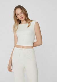 Bílý ribbed crop top s kulatým výstřihem, doplněný o odpovídající kalhoty na stažení. Tkanina je měkká s texturovaným povrchem.