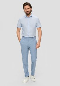 Camisa de botones de manga corta azul claro con un patrón de rayas sutil, combinada con pantalones ajustados azul claro y zapatillas blancas.