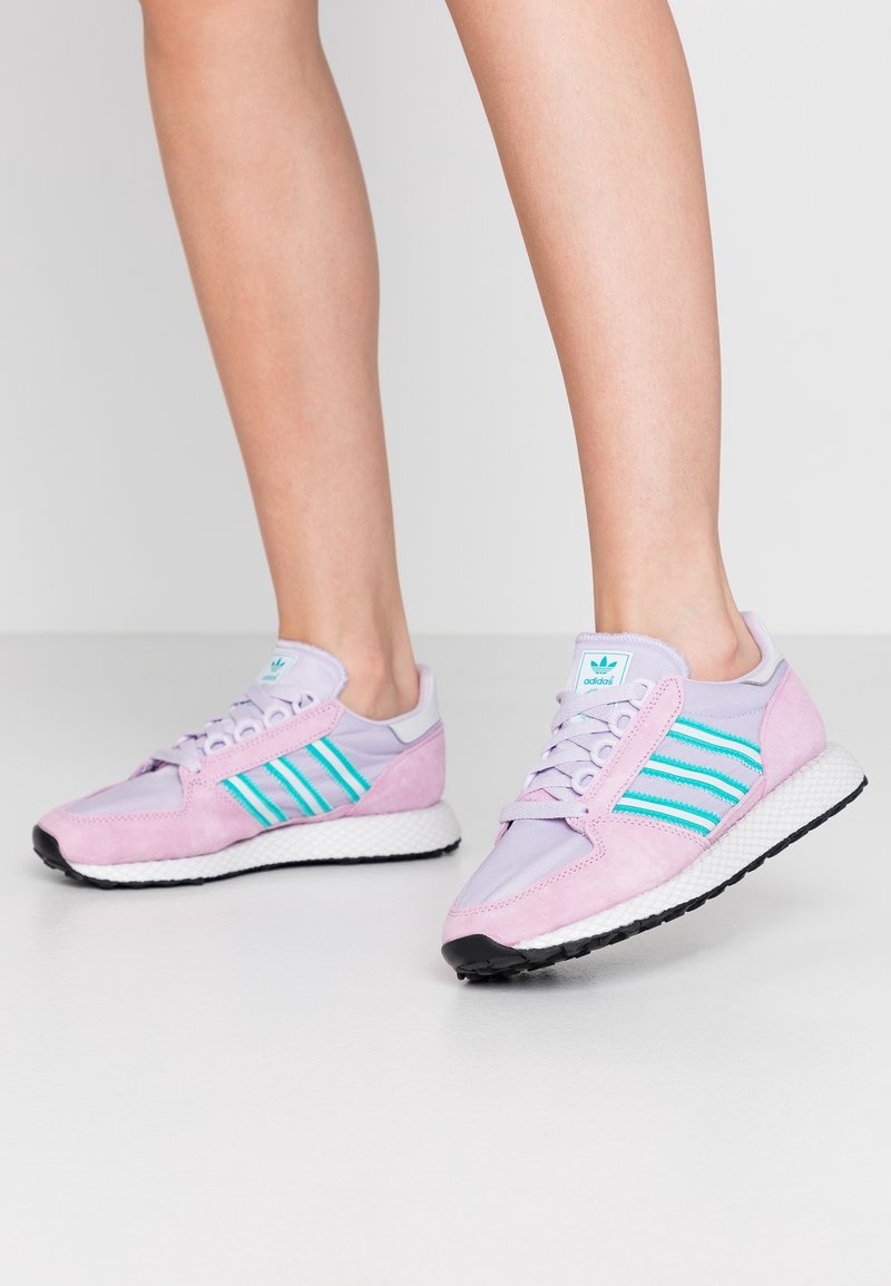 Des chaussures de sport violettes et roses en maille et en daim, avec trois bandes teal, une semelle intermédiaire blanche et une semelle extérieure en caoutchouc noir.