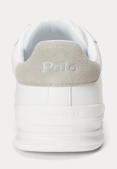 Balti sportiniai bateliai su pilku zomšiniu kulno lipduku, kuriame įspaustas užrašas „Polo“, ir baltu padu su įspaustu užrašu „Ralph Lauren“, matomi iš nugaros.