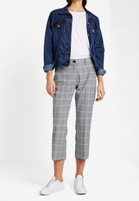 Džínová bunda přes bílé tričko. Šedé kostkované zkrácené kalhoty se světle modrými pruhy. Bílé tenisky dotvářejí celý outfit.