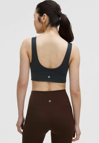 Donkergrijze sportbeha met brede bandjes en een ronde rug, gecombineerd met hooggewezene bruine legging, met een logo-detail op de tailleband.