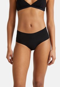 Donna che indossa mutandine nere seamless a vita media e un reggiseno nero abbinato, mostrata dalla metà del torso fino alla parte superiore delle cosce.