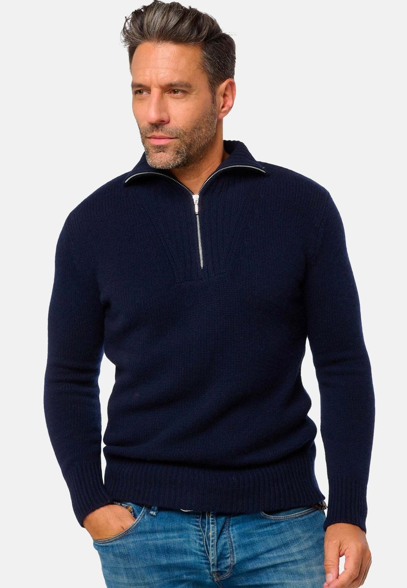 Pull en maille bleu marine avec col zippé, poignets et ourlet côtelés. Présente un design texturé sur le devant, mettant en valeur un style classique.