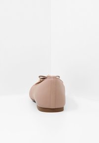 Ballerines en matériau synthétique rose doux avec un bout rond, un petit nœud décoratif et une semelle plate marron. Fini avec une texture lisse.