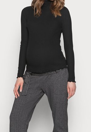 Femme portant un pull à col roulé noir à manches longues et un pantalon taille haute gris avec un motif chevron subtil.