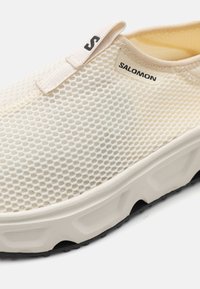 Baskets slip-on blanches en maille avec un empeigne texturée, semelle noire et marquage subtil. Présente un design arrondi et un matériau flexible.