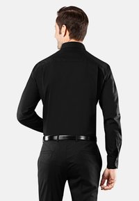 Camicia nera a maniche lunghe realizzata in tessuto morbido con una vestibilità su misura, dotata di polsini con bottoni e colletto alto, indossata con pantaloni eleganti neri.