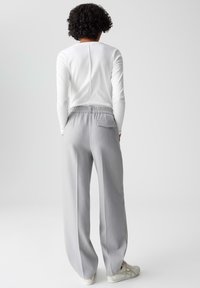 Light gray trousers with a relaxed fit, elastic waistband, and a back pocket, paired with a fitted white long-sleeve top.