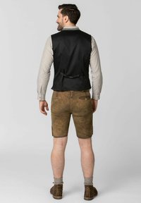 Schwarze Weste, kariertes Hemd, braune Ledershorts mit Taschen, beige knielange Socken und braune Schuhe. In abgewandter Position.
