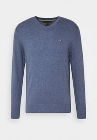 Maglione blu a V in tessuto morbido, con polsini e orlo a coste, e una piccola etichetta con logo sul petto.