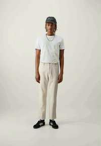 T-shirt blanche associée à un pantalon beige clair et des baskets noires avec des rayures blanches. Une casquette noire ajoute une touche à l'ensemble.