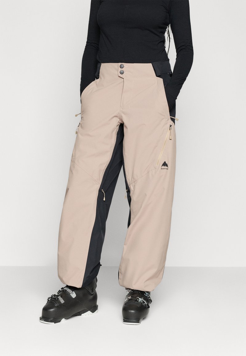 Pantaloni de schi impermeabili bej și bleumarin, cu talie ajustabilă, buzunare laterale și ventilație cu fermoar. Fabricat dintr-un material durabil, rezistent la intemperii.