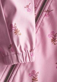 Tessuto di giacca rosa chiaro con polsino elasticizzato caratterizzato da motivi floreali in tonalità rosa scuro e marrone, e dettaglio di cerniera a contrasto.