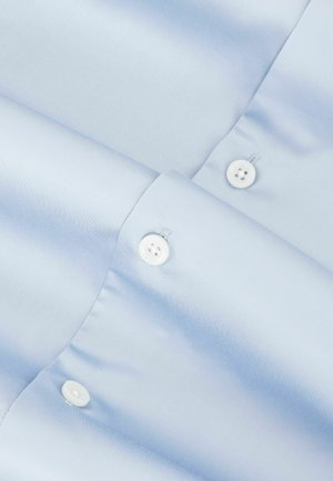 Camisa de satén azul claro con textura suave, con cierres de botones blancos y mangas dobladas. Diseño minimalista sin patrones.