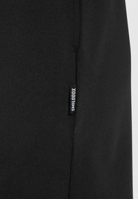 Sudadera negra con una textura de tela suave y una pequeña etiqueta de marca en el lateral. Diseño simple sin patrones ni acentos visibles.