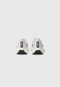 Une paire de chaussures de course blanches et noires vues de l'arrière sur un fond clair.