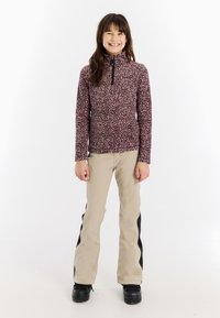 Ružový fleecový zipsový top s čiernym vzorom leopardu, skombinovaný s béžovými nohavicami s čiernymi bočnými pruhmi a čiernymi bootmi.