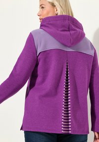 Sudadera morada con paneles acanalados y una apertura trasera a rayas. Cuenta con una capucha ajustable y aberturas laterales. Textura suave, diseño informal.