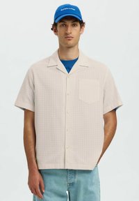 Korte mouwen, lichtbeige button-up shirt met een ruitpatroon en een enkele zak. Draag het over een blauw T-shirt met ronde hals en combineer het met lichte spijkerbroeken.