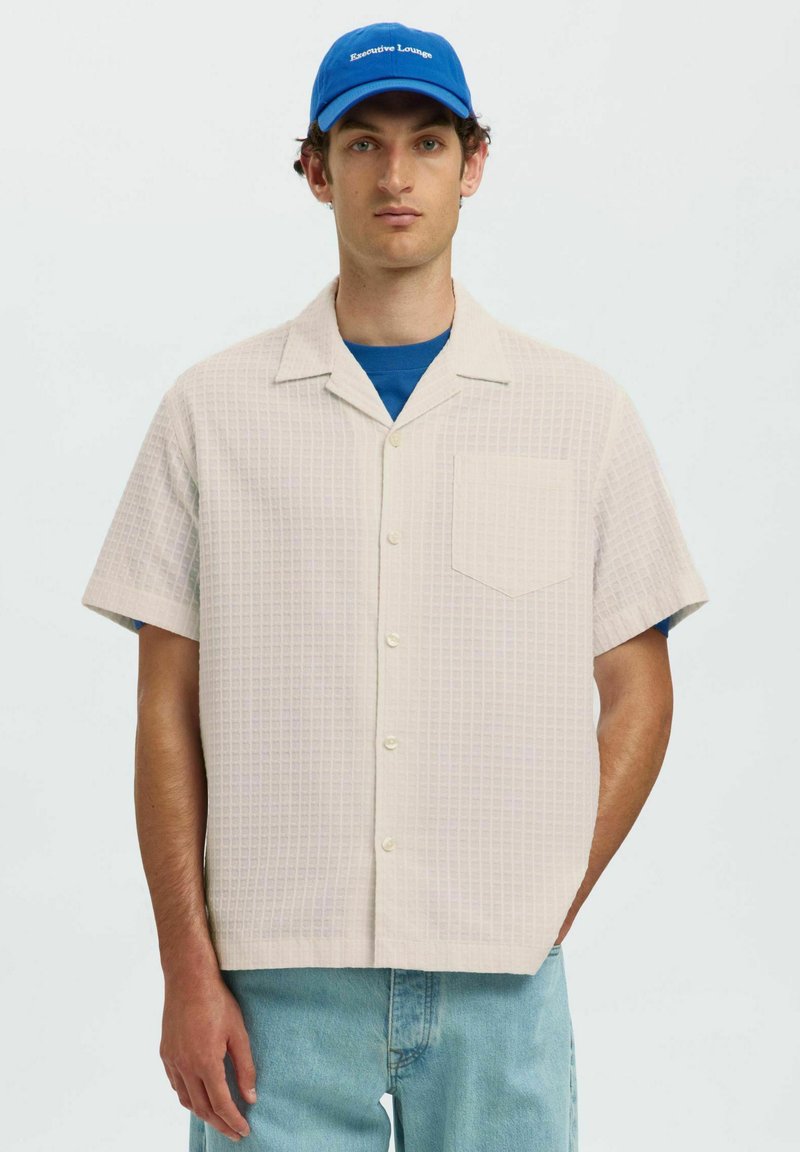 Korte mouwen, lichtbeige button-up shirt met een ruitpatroon en een enkele zak. Draag het over een blauw T-shirt met ronde hals en combineer het met lichte spijkerbroeken.
