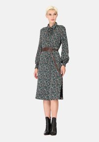Robe à motifs floraux de couleur vert foncé avec une taille cintrée et une ceinture marron, dotée de manches longues et d'une silhouette A-line mi-longue.