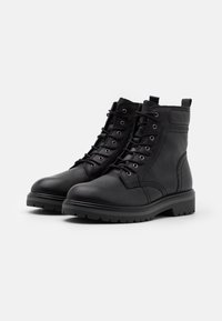 Botas de tobillo de cuero negro con diseño de cordones, punta redonda, parte superior texturizada y suela de tacos para tracción. Incluye ojales de metal y detalles de costura.