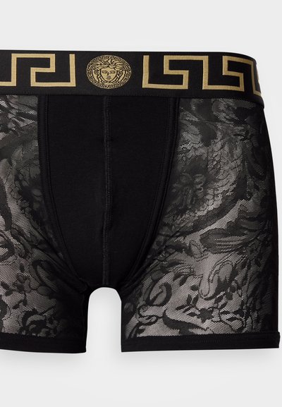 Μαύρα ανδρικά εσώρουχα μποξέρ με διαφανή δαντέλα και ανθικά σχέδια, με σταθερή ζώνη μέσης διακοσμημένη με χρυσό μοτίβο σε ελληνικό στυλ.
