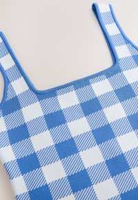 Top de punto con patrón de cuadros en azul y blanco. Presenta tirantes gruesos y un escote cuadrado. Textura suave con franjas alternadas.