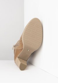 Bottine beige avec une semelle en caoutchouc texturée, fermeture éclair et un talon modéré. Tige en cuir lisse avec des détails de couture.