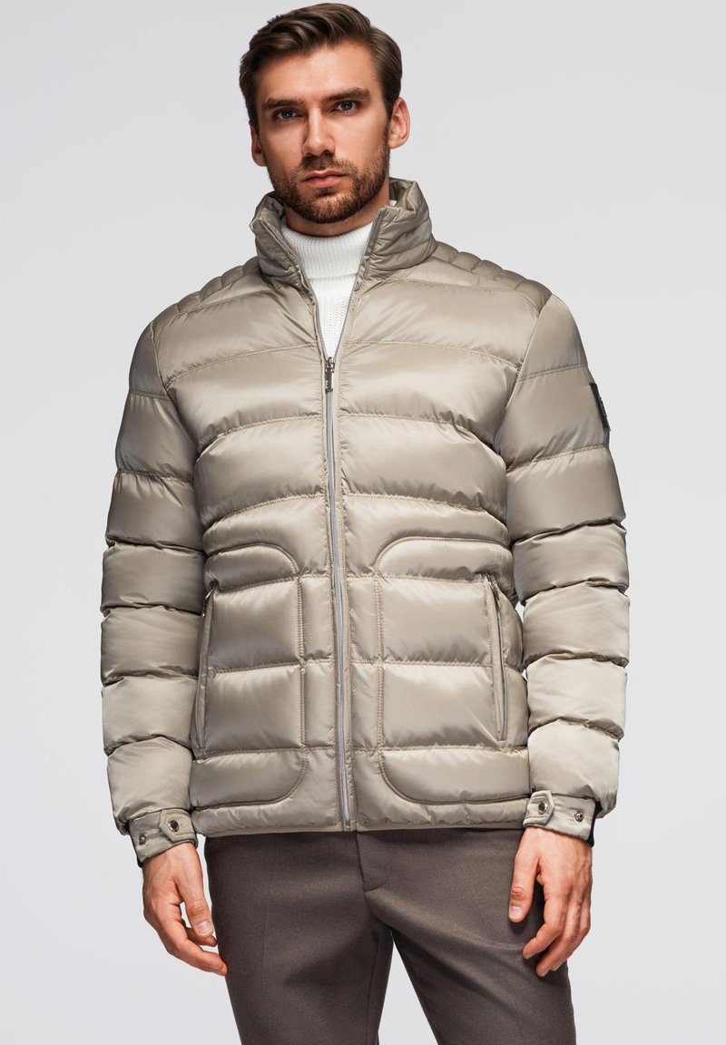 Lys beige pufferjakke med høj krave, quiltet design, lynlås foran og sidelommer. Glat, skinnende stof med fitted ærmer.