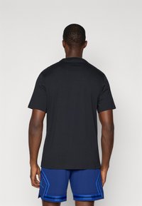 Czarna, krótko rękawowa koszulka z bawełny, z okrągłym dekoltem i prostym krojem, noszona z niebieskimi szortami sportowymi z bocznymi paskami.