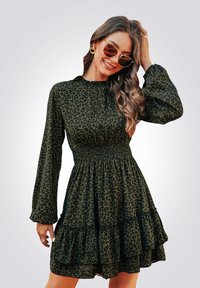 Abito verde con stampa leopardata, maniche lunghe, vita arricciata e orlo a volants. Presenta un collo alto e un tessuto leggero.