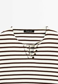 Close-up of a brown and white striped shirt neckline with four small buttons on one side and a brand label at the collar.
