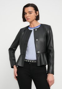 Μαύρο μπουφάν από δερματίνη με peplum τελείωμα, διακοσμημένο με ασημί κουμπιά κλικ, μακριά μανίκια και στρογγυλεμένο λαιμό, φορεμένο πάνω από ριγέ τοπ.