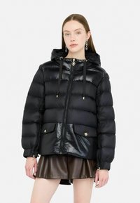 Giacca imbottita nera con finitura lucida, cappuccio, accessori dorati, chiusura con zip e due tasche frontali. Superficie testurizzata con motivo trapuntato.