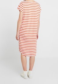 Pasiasta sukienka w kolorze białym i pomarańczowym, o luźnym kroju, z krótkimi rękawami i rozcięciem po bokach. Noszona z białymi botkami za kostkę.