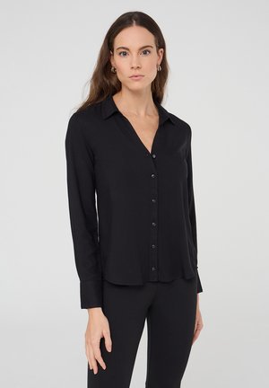 Camicia nera con bottoni, maniche lunghe, tessuto morbido, colletto classico e patta frontale. Presenta un orlo arrotondato e un design minimalista.