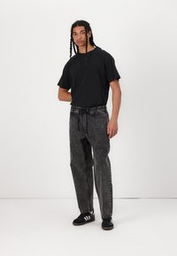 Black short-sleeve t-shirt paired with loose-fit, faded black jeans. Textured denim, elastic waistband, and tonal stitching. Black sneakers with white stripes.