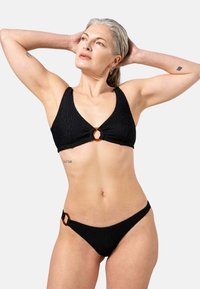 Zwart bikini set met textuurstof, een driehoekige bralette met een ronde oranje hardware-detail, en bijpassende lage slipjes.