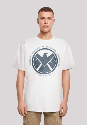 Hvit bomullst-skjorte med en stor sirkulær grafikk som har et mørkt emblem og tekst: "Strategic Homeland Intervention Enforcement Logistic Division."