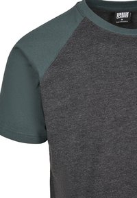Harmaa T-paita tummanvihreillä raglan-hihoilla, valmistettu pehmeästä puuvillasekoitekuidusta, jossa on pyöreä kaula-aukko ja kontrastoivia tekstuureja.