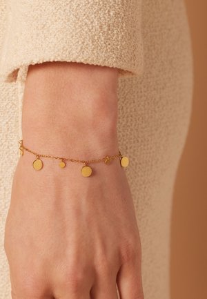 Gouden armband met meerdere hangende ronde bedels, variërend in grootte. Gladde, reflecterende oppervlakken en delicate ketting schakels.