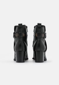 Bottines en cuir noir avec un bout rond, un talon épais en bloc, une fermeture éclair sur le côté, et un détail de boucle. Présente une finition texturée et des accents de couture.